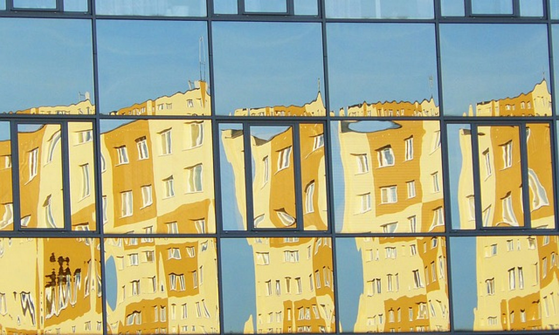 Eine verspiegelte Wand, in der sich ein großes Wohngebäude spiegelt.