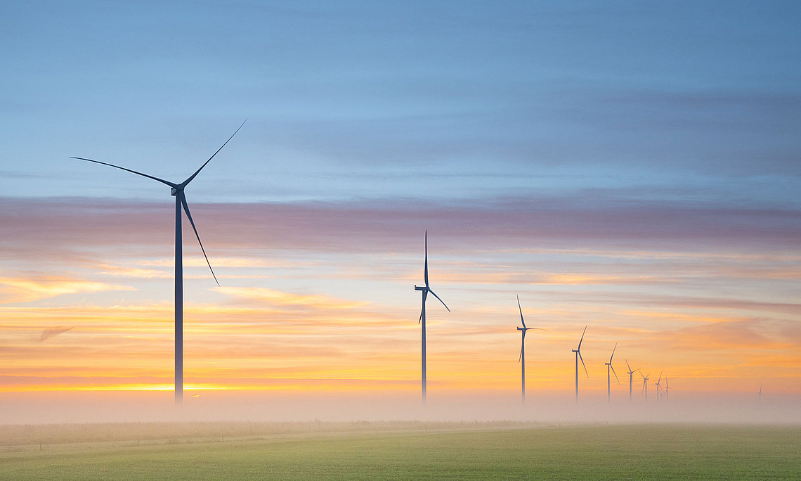 Windräder auf grüner Wiese mit Nebel, Abendstimmung mit orangen Wolken