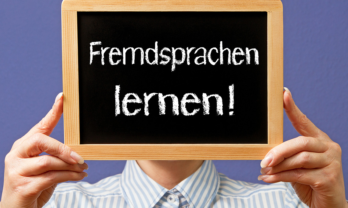 Eine Person hält ein Schild mit der Aufschrift "Fremdsprachen lernen!"