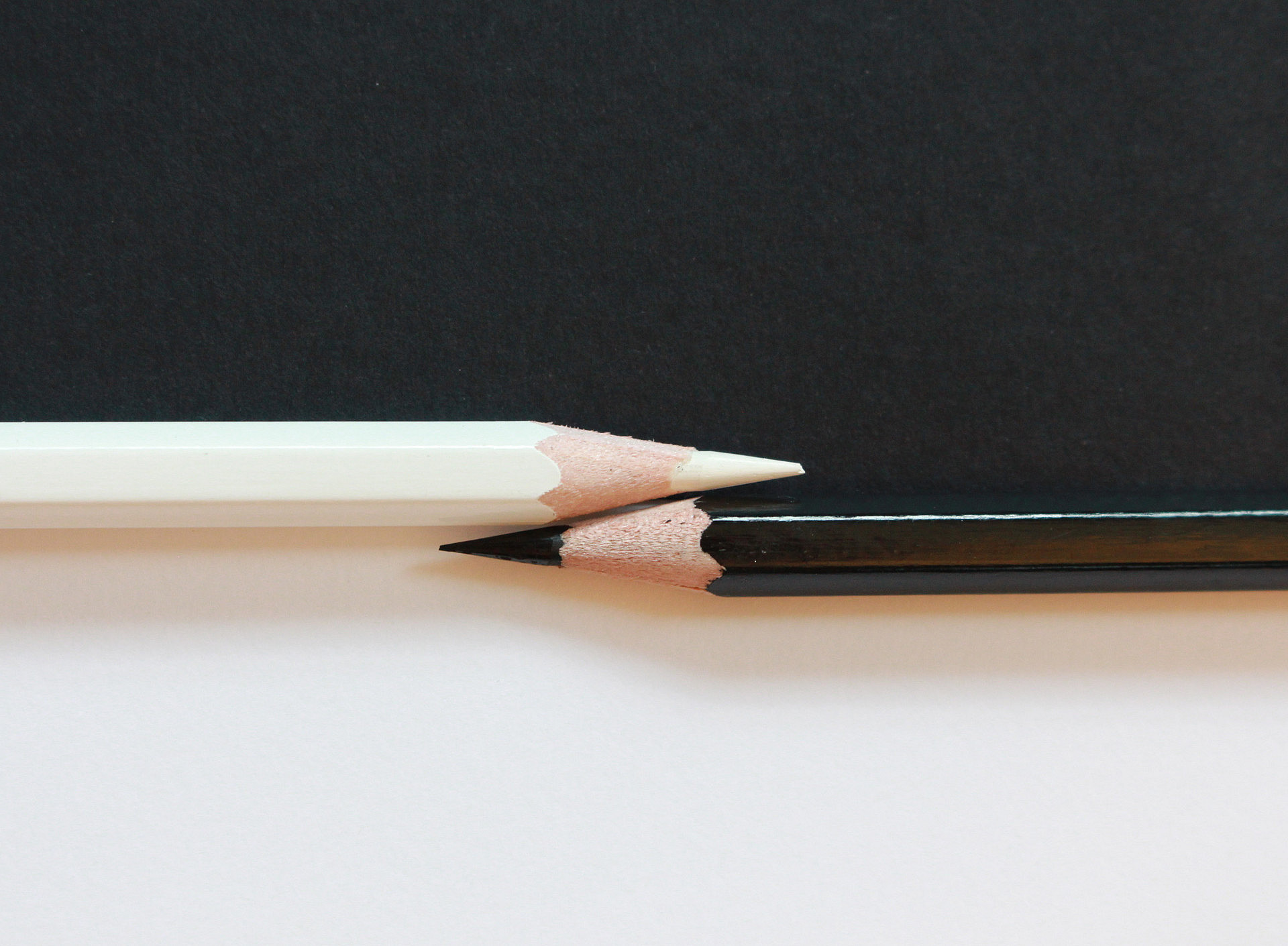 ein schwarzer und ein weißer Buntstift, die zueinander zeigen, vor einem schwarz-weißen Hintergrund 