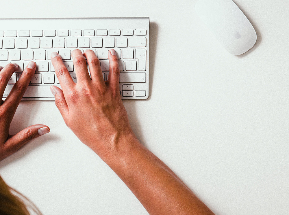 Person, die auf Apple Cordless Keyboard tippt und neben ihr liegen eine gelbe Uhr und ein Handy ©by Damian Zaleski on unsplash