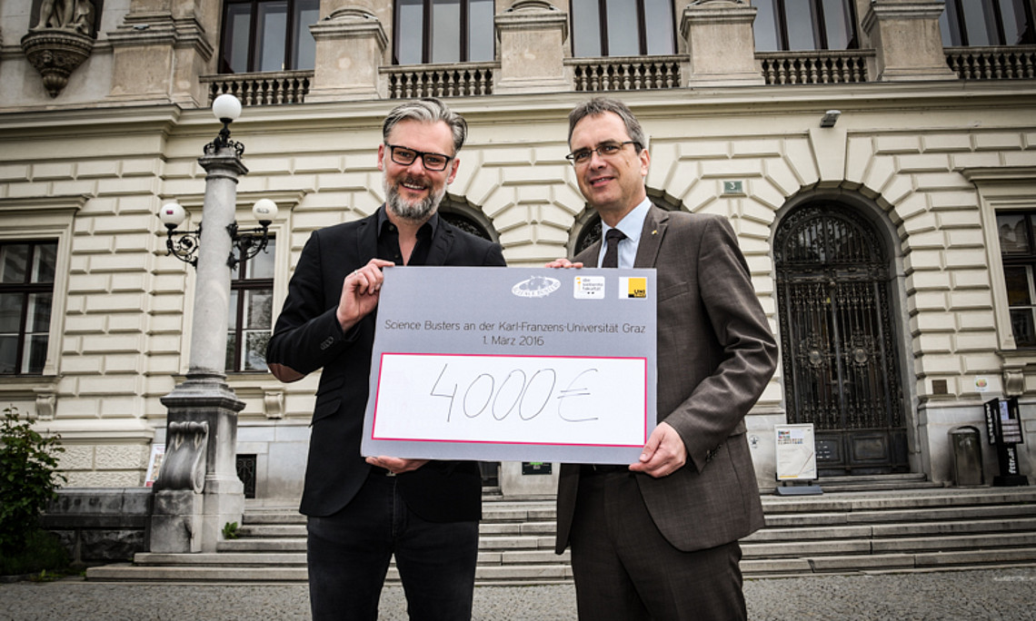 Science-Buster Helmut Jungwirth übergibt an Vizerektor Peter Riedler einen Scheck in der Höhe von 4000 Euro. Die 7. fakultät, die den Abend veranstaltete, spendet den Betrag für den Flüchtlingsfonds der Universität Graz. Foto: Uni Graz/Tzivanopoulo