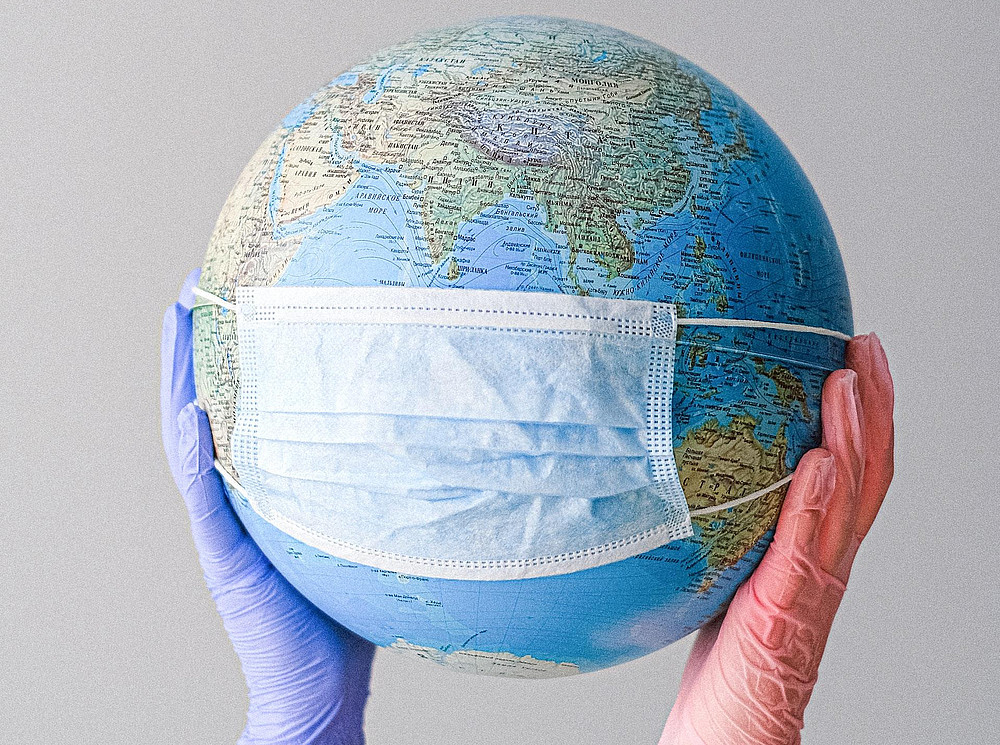 Globus mit Maske, der von zwei Händen mit Handschuhen getragen wird ©Anna Shvets