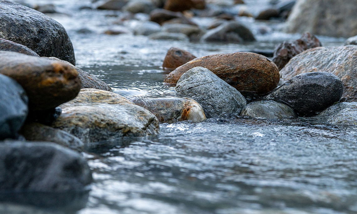 fließendes Wasser in einem Bachbett mit großen rund geschliffenen Steinen