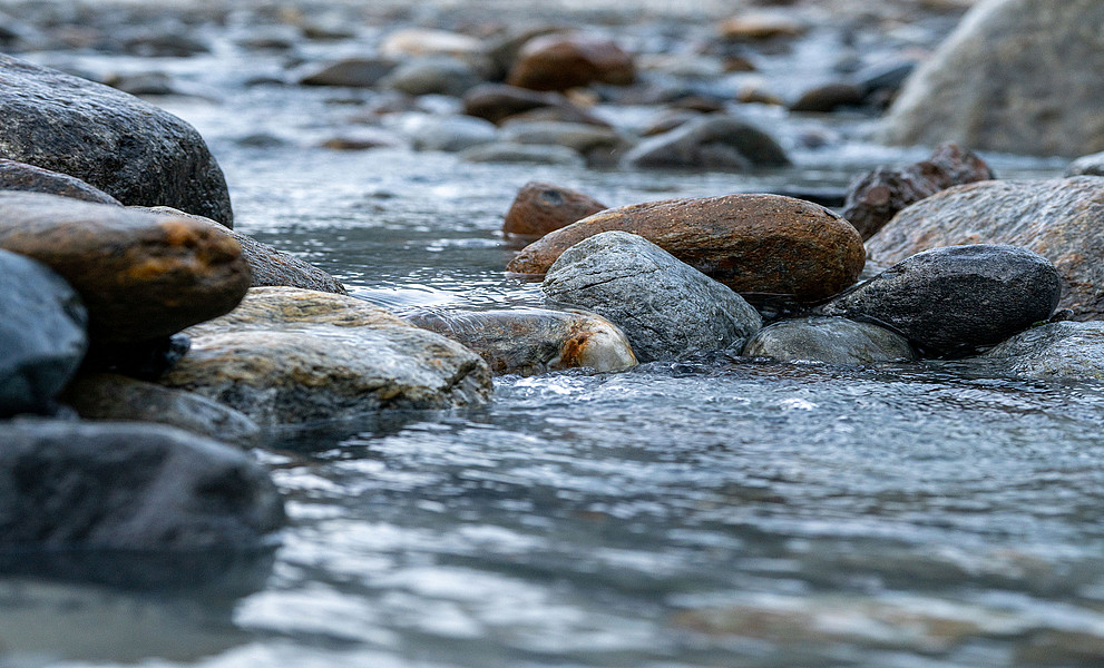 fließendes Wasser in einem Bachbett mit großen rund geschliffenen Steinen