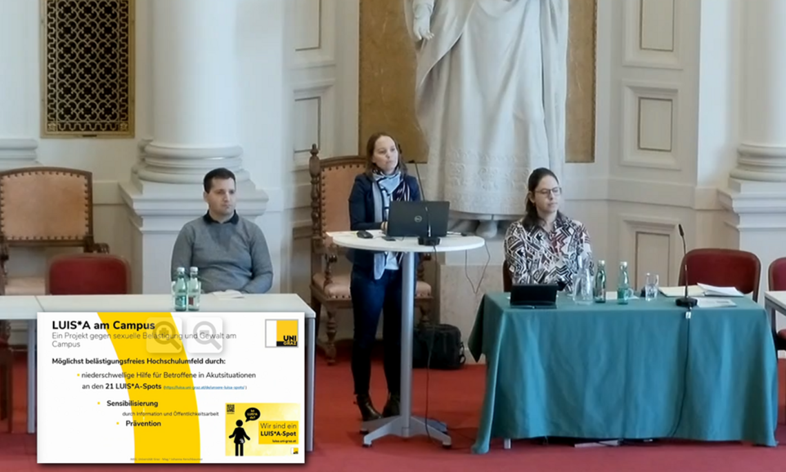 Drei Personen in der Grazer Aula sitzen bzw. stehen an einem Pult und Tisch, um im Rahmen des Sicherheitstages Projekte vorzustellen