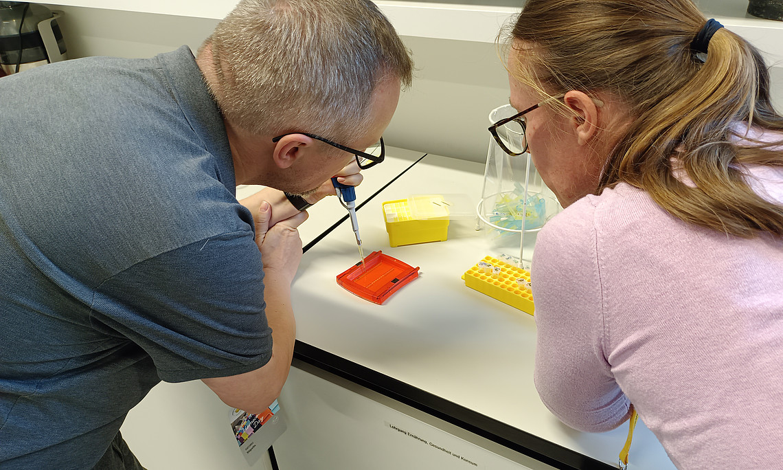 ein Mann und eine Frau von hinten fotografiert, stehen an einem Labortisch und experimentieren