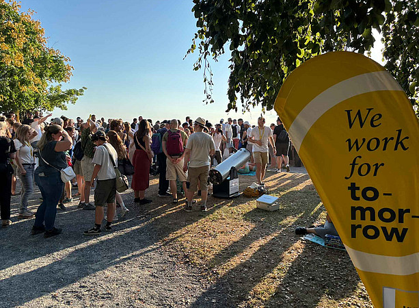 Menschen auf dem Schloßberg, auf einem Bech Flag ist We work for tomorrow zu lesen 