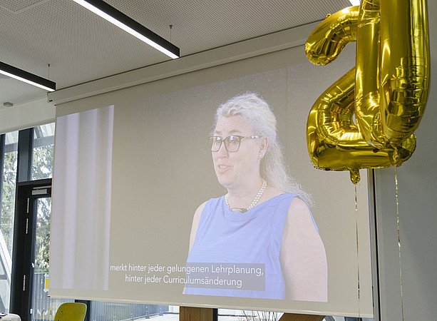 Eine Frau in blauem Kleid spricht auf einer Videoleinwand bei einer Veranstaltung; neben ihr hängen goldene Luftballons in Form der Zahl 20. ©@foto-gasser.at