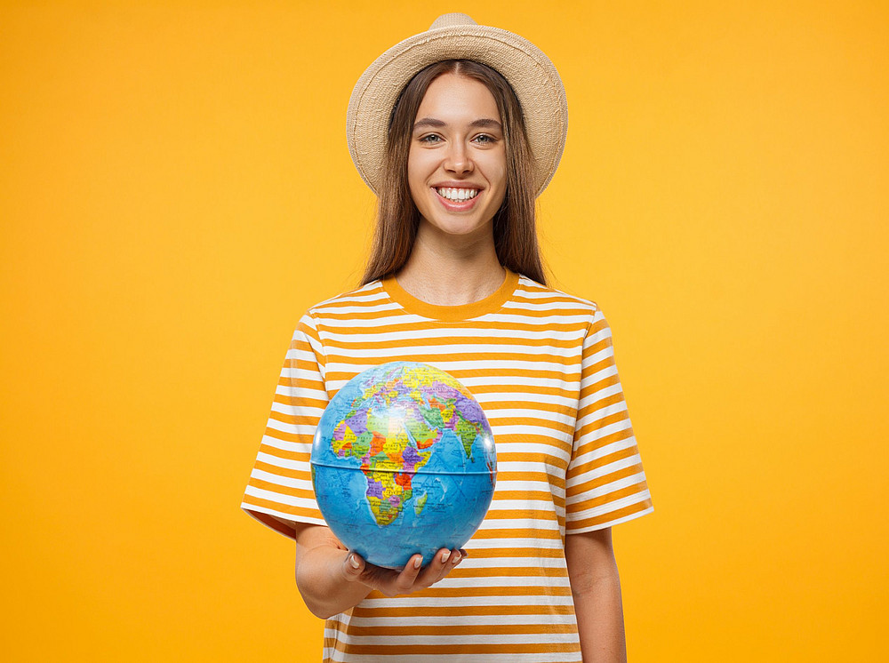 Studieren im Ausland © Damir Khabirov - stock.adobe.com Young woman against a yellow background holding a globe in her hand. {f:if(condition: ' Damir Khabirov - stock.adobe.com', then: '© Damir Khabirov - stock.adobe.com')}