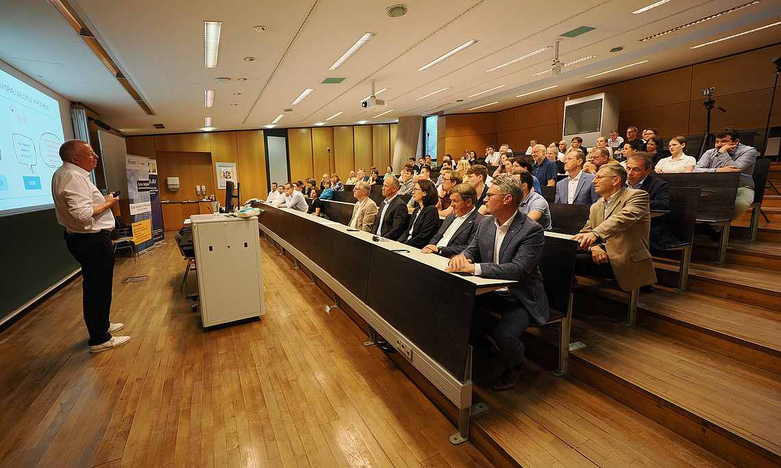 Eine Person in einem Hörsaal hält eine Präsentation vor einer Gruppe von Menschen