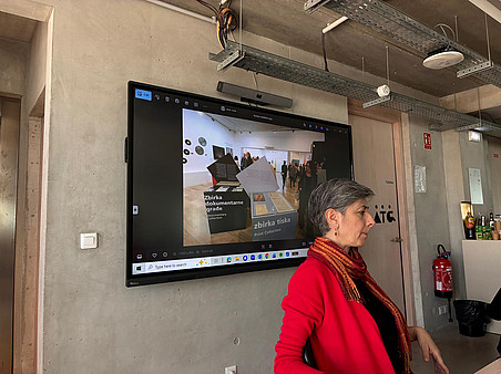 A woman in a red sweater sitting in front of a big screen ©Ben Gidley