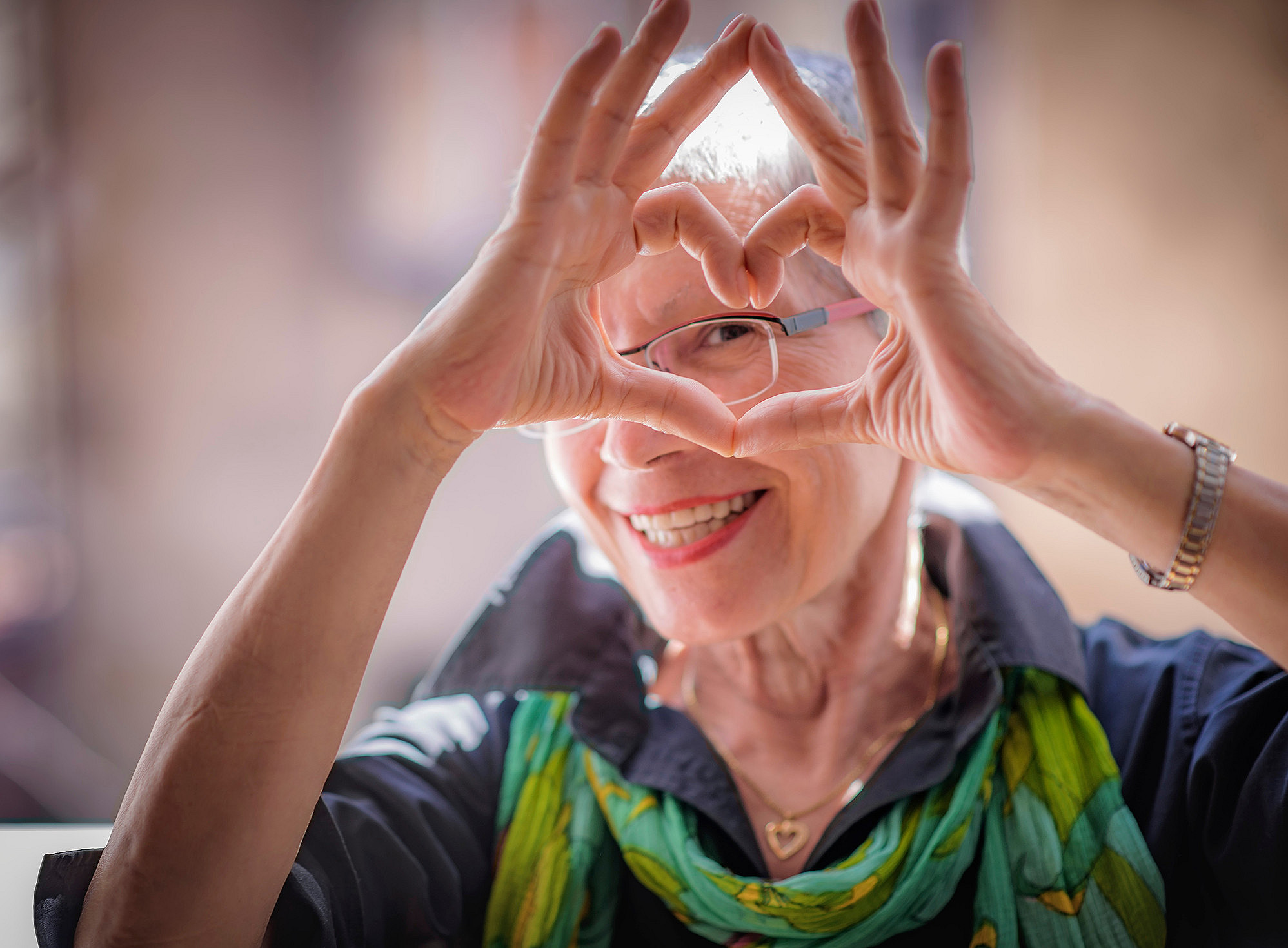 ältere Dame mit Brille macht mit ihren Fingern ein Herz und blickt durch ©Teodor Lazarev - stock.adobe.com