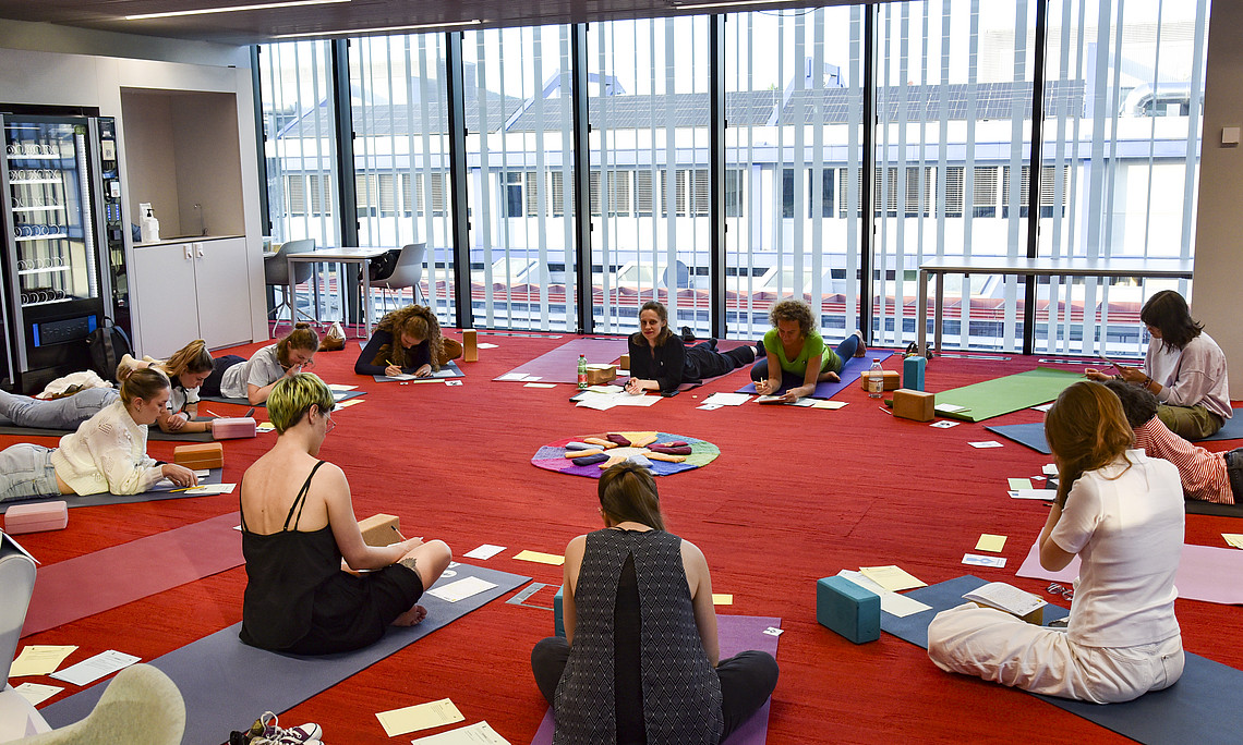 Personen sitzen am Boden auf Yogamatten