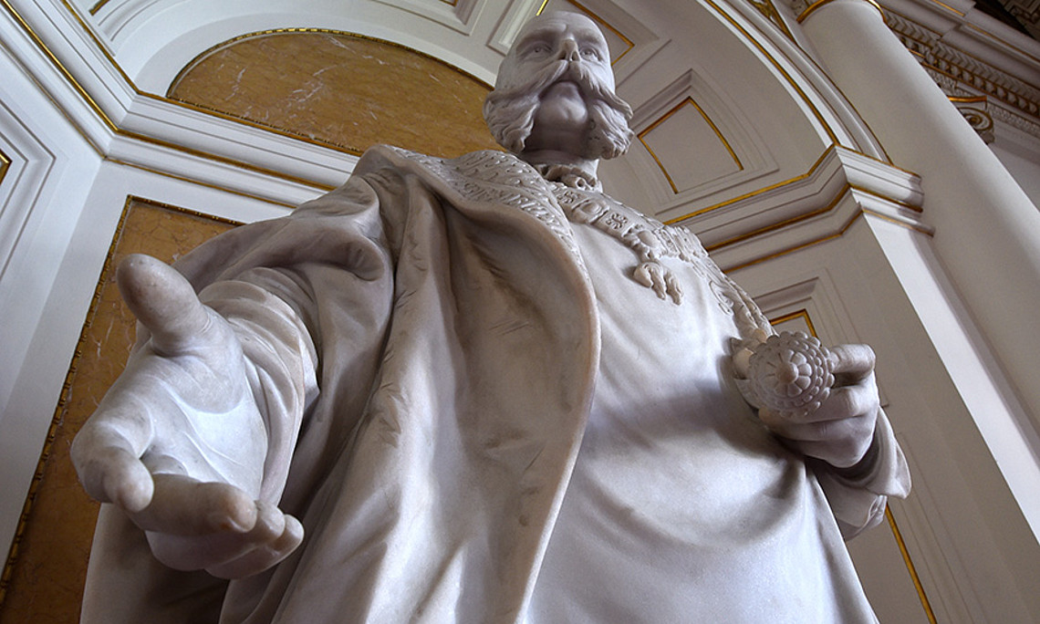 Ö1-Journalist Martin Haidinger und Historiker Peter Teibenbacher erzählen vor der Statue des bis heute präsenten Monarchen in der Aula der Uni Graz „die Österreich-Story“. Foto: Uni Graz/Schweiger 