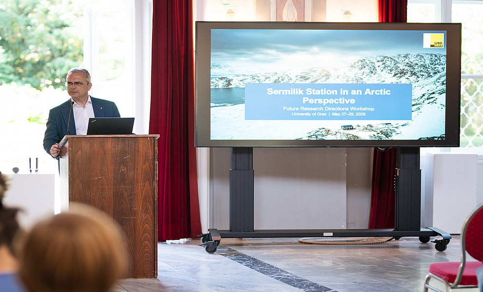 Eine Person im Anzug spricht zum Publikum, im Hintergrund sieht man ein großformatiges Bild von schneebedeckten Bergern und der Aufschrift "Sermilik Station in an Arctic Perspective"