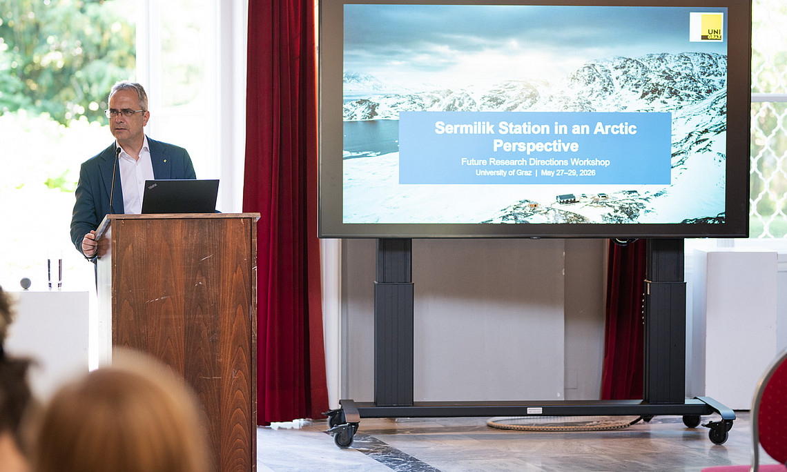 Eine Person im Anzug spricht zum Publikum, im Hintergrund sieht man ein großformatiges Bild von schneebedeckten Bergern und der Aufschrift "Sermilik Station in an Arctic Perspective"
