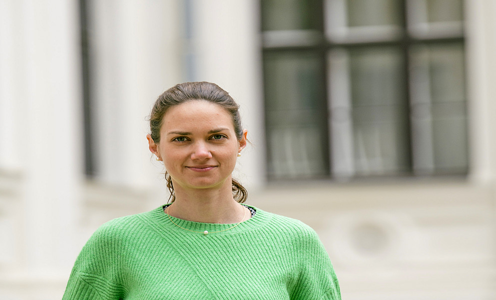 Eine Frau hat einen grünen Pullover an und steht im Innenhof der Uni Graz