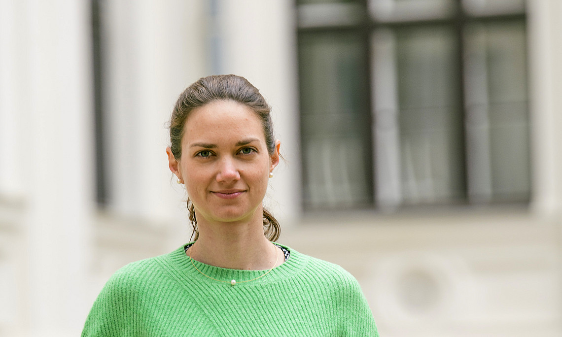 A woman wears a green sweater and stands in the inner courtyard of the University of Graz