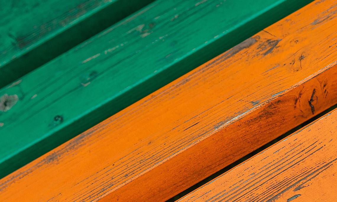 die Sitzfläche einer Bank mit grünem und dann orangenen Holz wird gezeigt