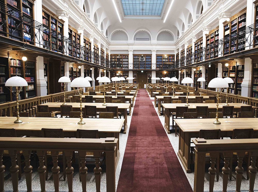 The historic reading room of the University Library at the University of Graz. The room contains rows of tables, table lamps and bookshelves ©Uni Graz/Tzivanopoulos