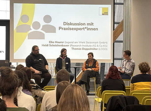 drei Frauen und ein Mann sitzen vor einer Leinwand und sprechen miteinander; im Publikum sitzen viele Menschen und hören zu ©Uni Graz/Schmieder