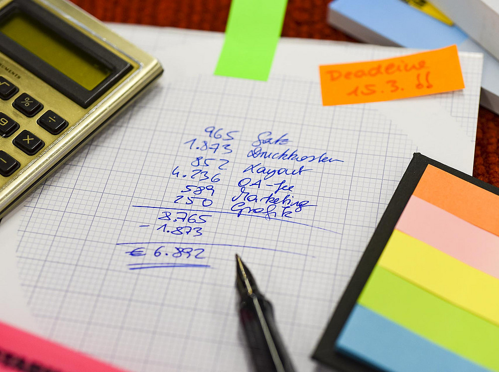 A calculation on a sheet of paper - pen, post-its, calculator are also seen. ©Uni Graz/Schwarz