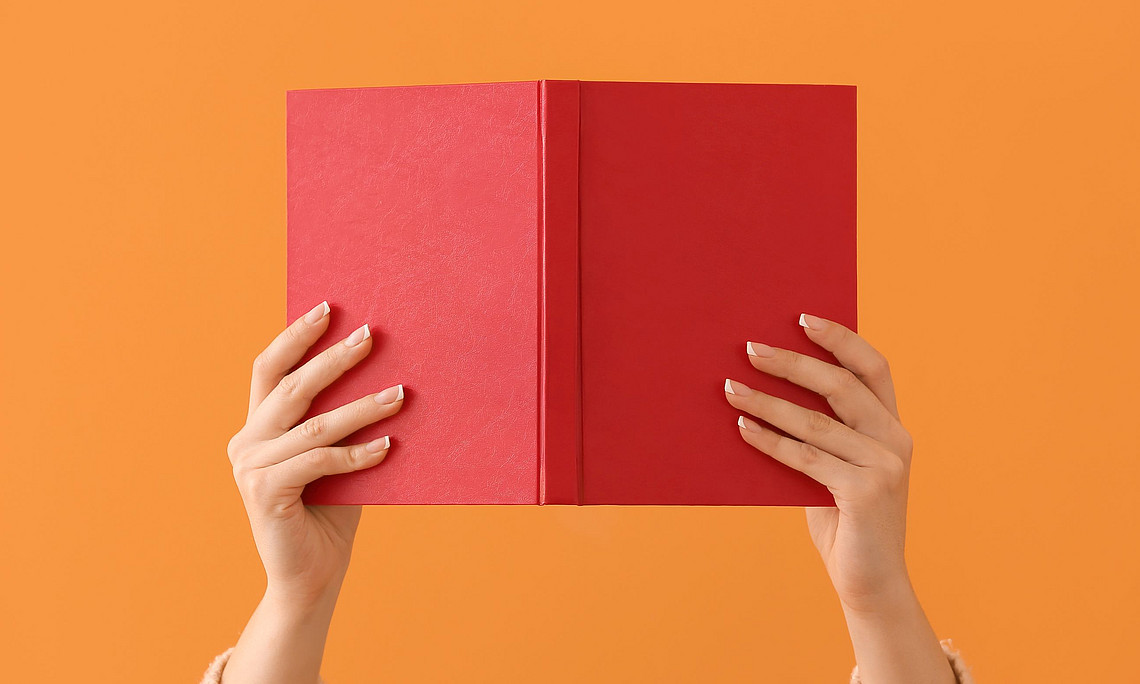 Hände halten vor einem orangen Hintergrund ein Buch hoch