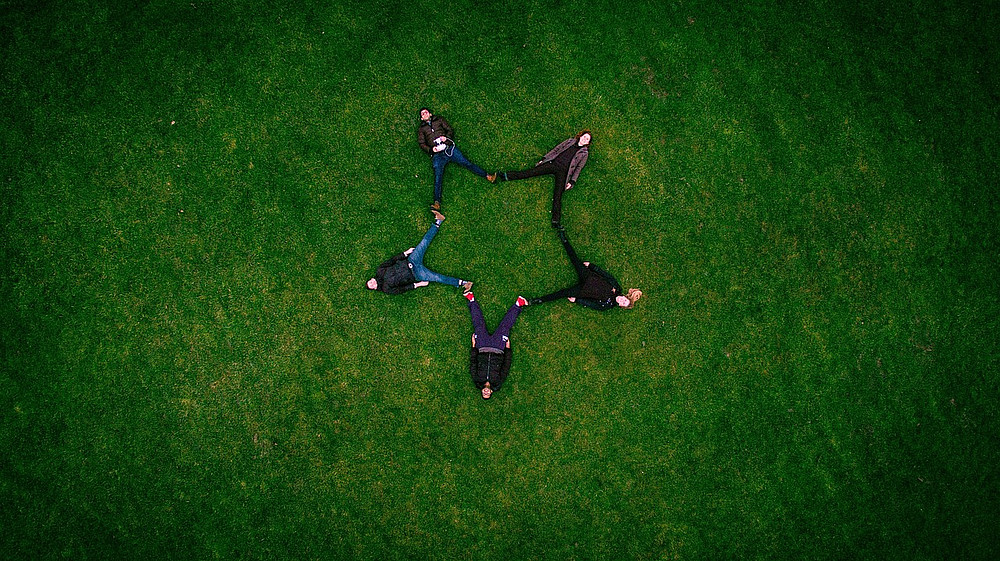 Fünf Personen aus der Vogelperspektive, die im Gras liegen und ihre Beine so aneinanderhalten, dass die Form eines Sterns gebildet wird ©Pexels | Pixabay