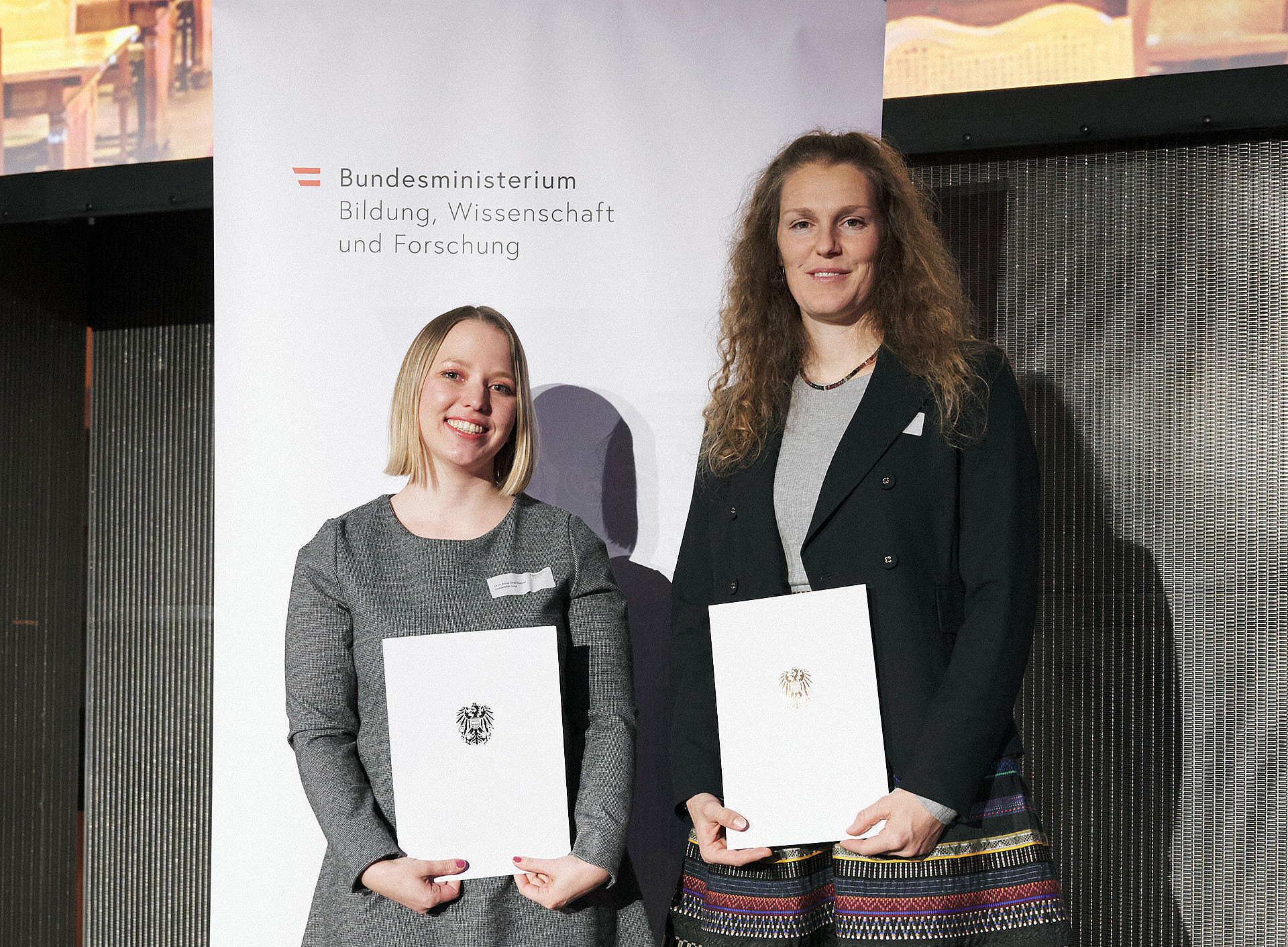 Anna Graf-Steiner und Marina Maren Reiner mit Urkunden vor einem Roll-up des BMBWF ©eap.at | Gerry MAYER-ROHRMOSER