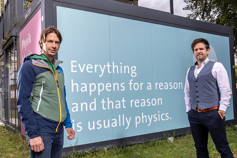 Alexander Bergmann und Peter Banzer vor dem Info-Point zum entstehenden Graz Center of Physics mit der Aufschrift Everything happens for a reason and that reason is usually physics". 