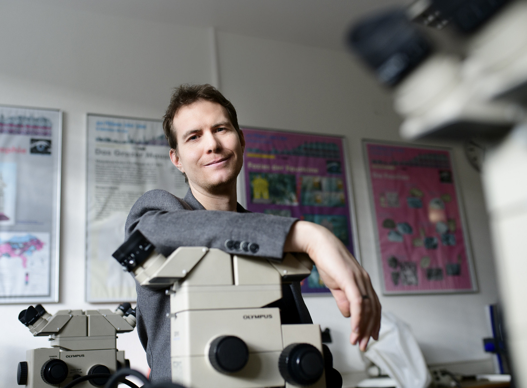 Erdwissenschaftler Gerald Auer lehnt über einem Mikroskop. ©Uni Graz/Tzivanopoulos