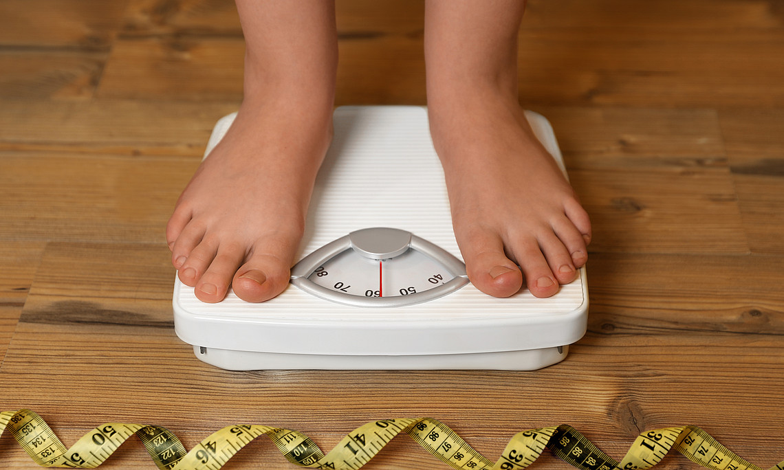 Two feet are standing on a scale, with a measuring tape in front of it.