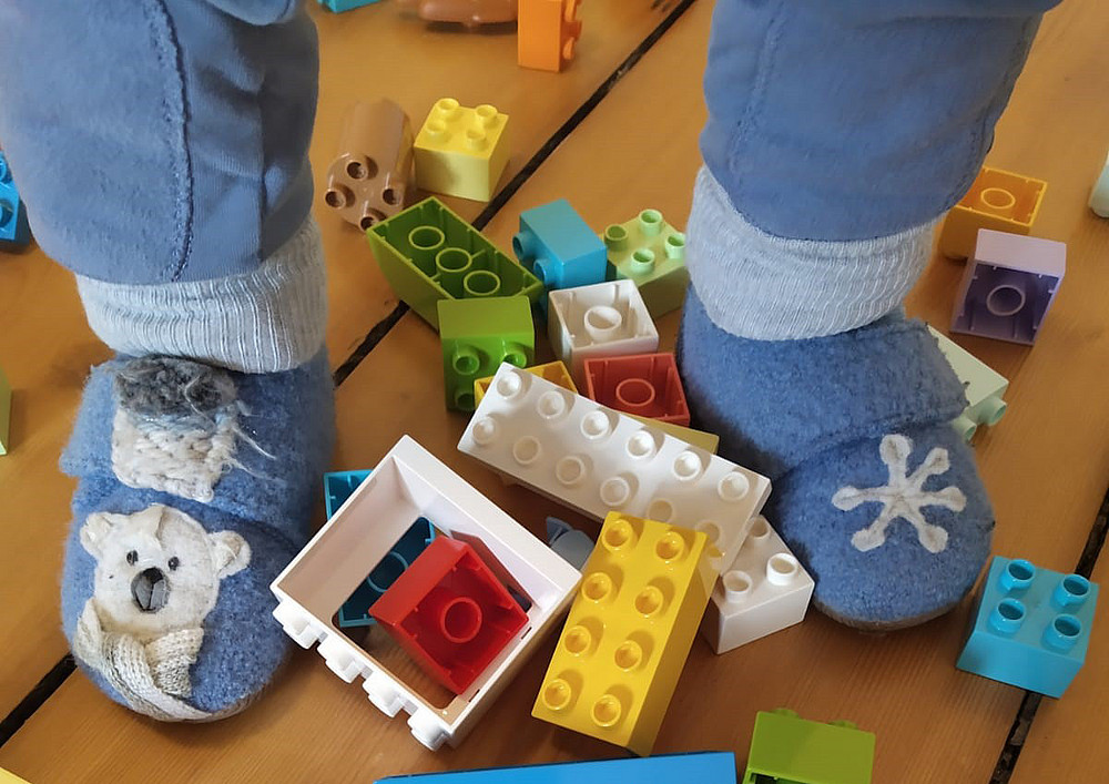 Füße eines Kleinkindes, die von bunten Legosteinen umgeben sind symbolisieren die Kinderbetreuung. ©Betriebstagesstätte Uni Graz