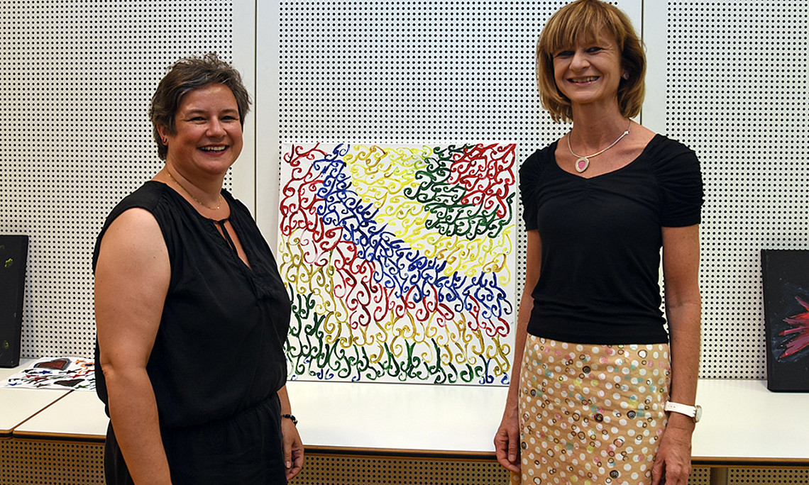 Verena Gallob von der Caritas und Maria Elisabeth Aigner vor einem Gemälde, das in der Lehrveranstaltung entstanden ist.