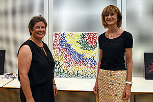 Verena Gallob von der Caritas und Maria Elisabeth Aigner vor einem Gemälde, das in der Lehrveranstaltung entstanden ist.