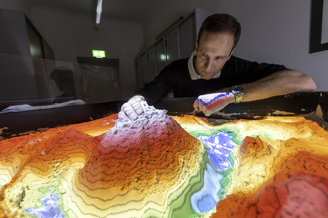 Mann neben dem Modell eines Berges symbolisiert das Bachelorstudium Geowissenschaften