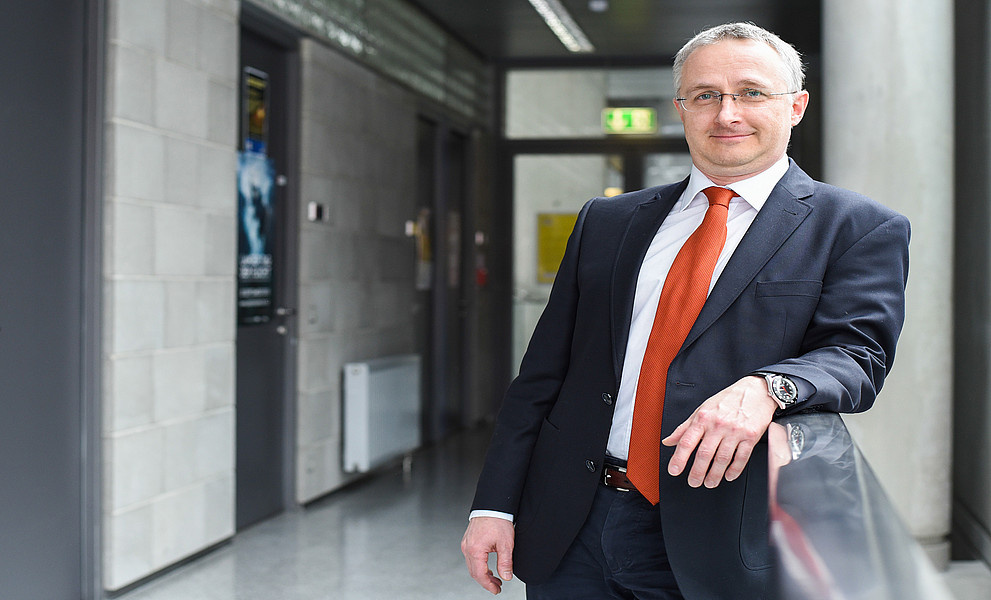 Gerd Oberleitner am Gang im RESOWI-Zentrum, mit Sakko und Krawatte, den linken Arm auf dem Geländer