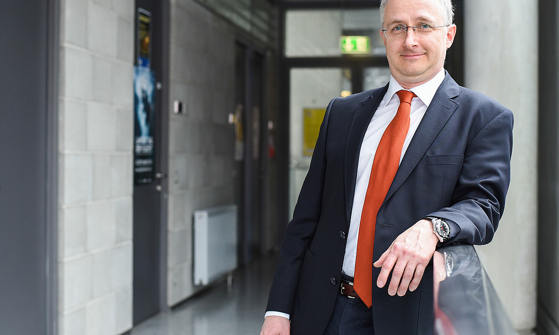 Gerd Oberleitner in the corridor of the RESOWI Centre, wearing a jacket and tie, his left arm on the railing
