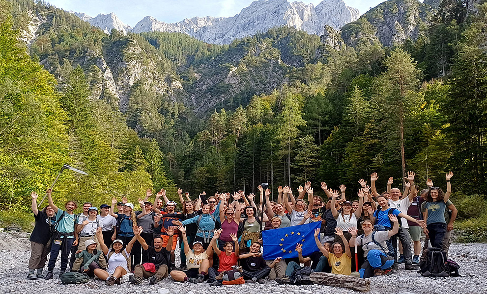Studierendengruppe - rund 50 Personen - in einem Tal, dahinter eine Bergkulisse, im Nationalpark Gesäuse