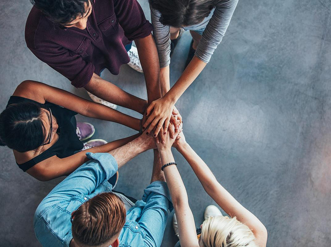 Five people form a semi-circle and put their hands in the middle so that they can place them on top of each other as a sign that they are a team. ©Jacob Lund - stock.adobe.com