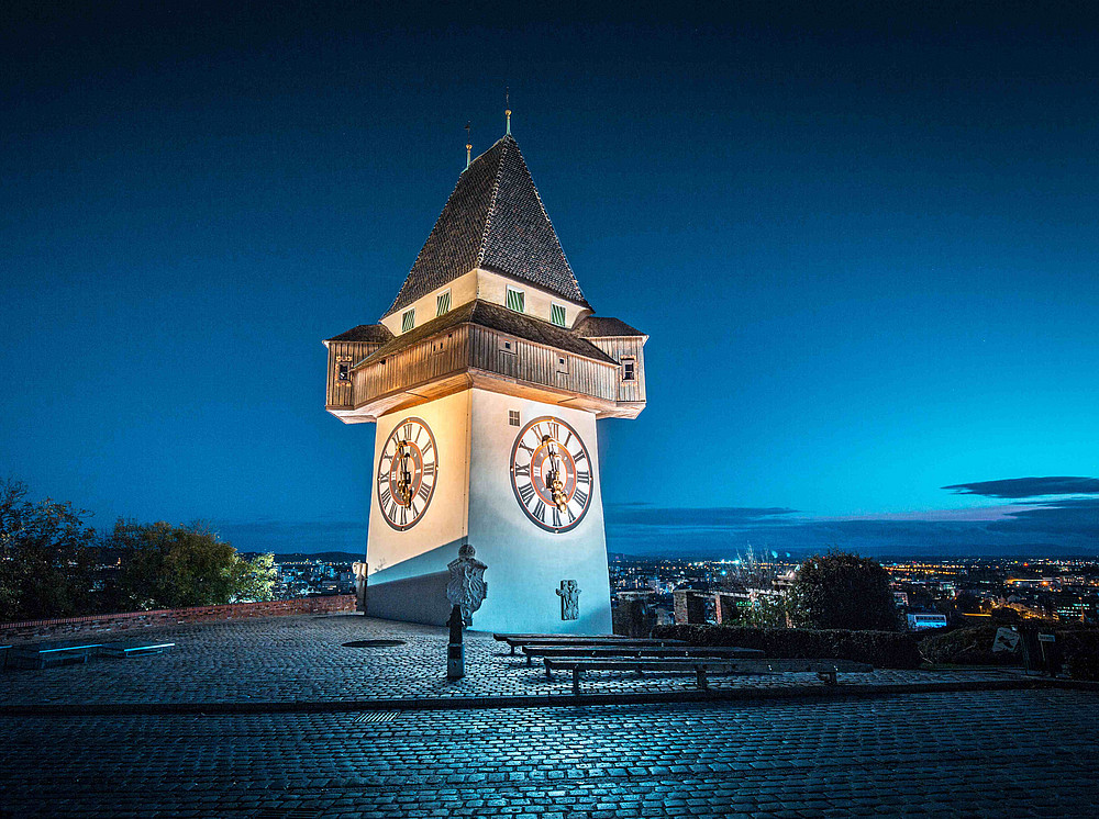 Grazer Uhrturm bei Nacht, der Nachthimmel über der Stadt im Hintergrund schimmert blau und symbolisiert das Projekt Stadtsprachen - Städte und ihre sprachlichen Strahlkräfte ©JFL Photography - stock.adobe.co