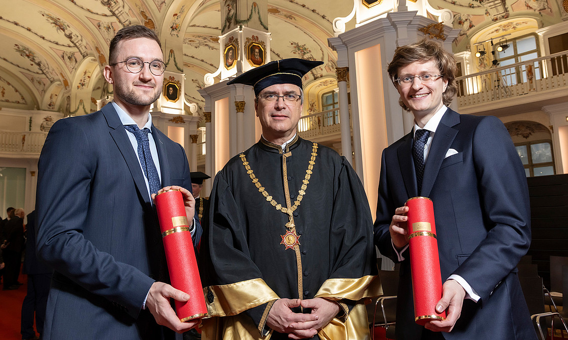 Rector Peter Riedler in the university gown with Andreas Habring and Andreas Windischbacher, holding their doctoral scrolls, in the auditorium of the Old University