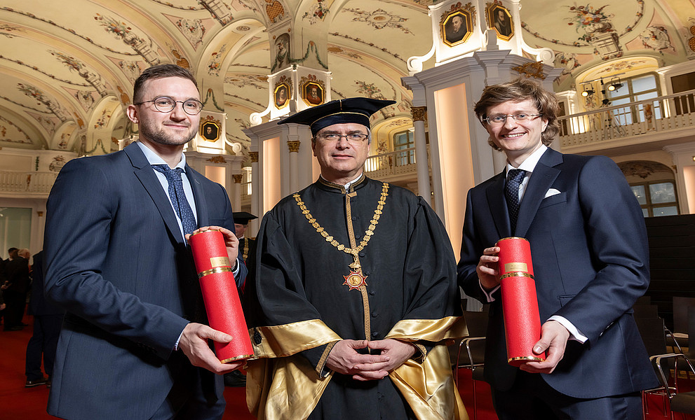 Rektor Peter Riedler im Talar mit Andreas Habring und Andreas Windischbacher, die ihre Promotionsrolle in der Hand halten, in der Aula der Alten Universität