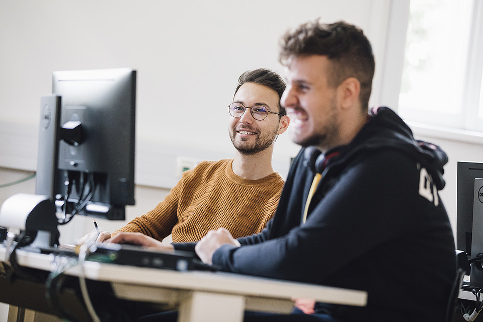Zwei Studierende schauen gemeinsam lachend auf einen Computerbildschirm.