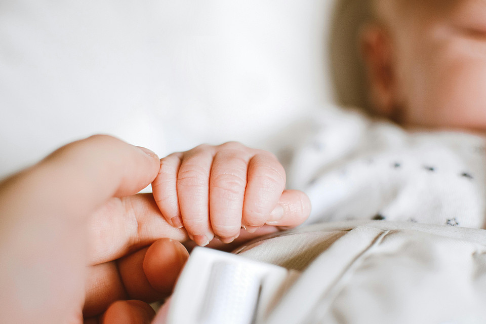 Eine Erwachsenenhand hält die Hand eines liegenden Babys