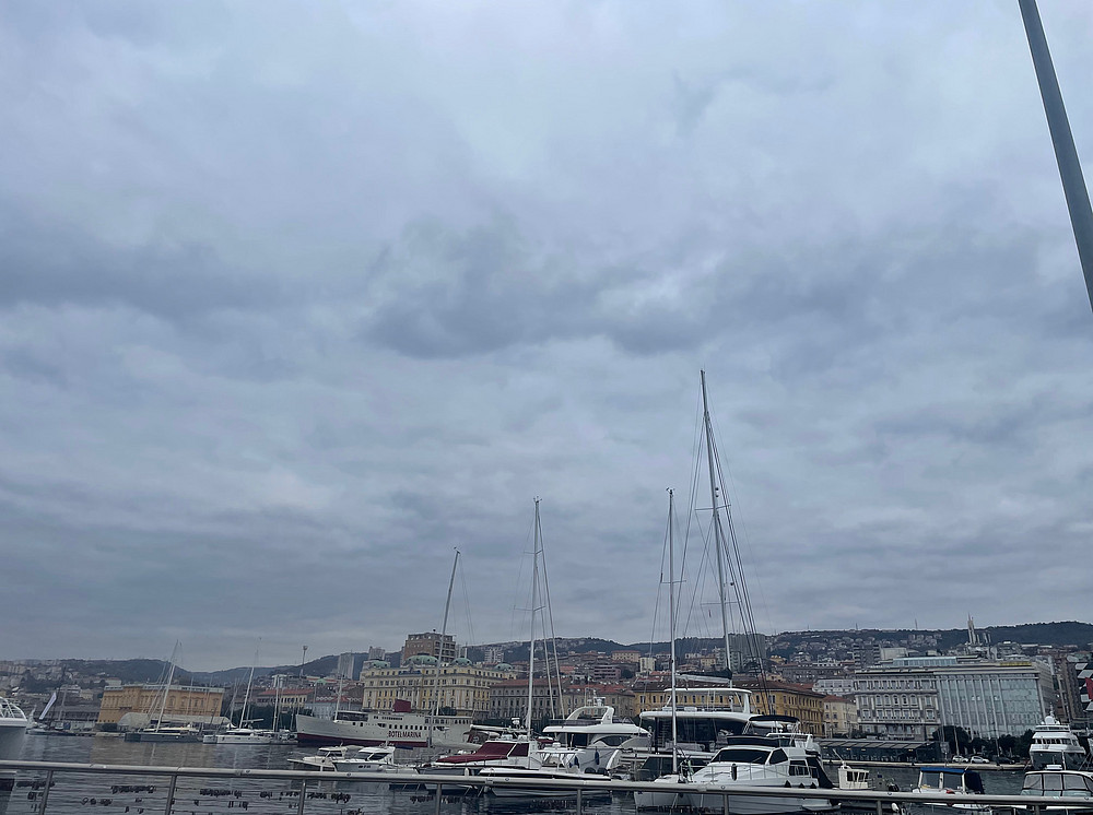 Das Bild zeigt den Hafen von Rijeka in Kroatien. Rijeka ist der wichtigste Hafen und die drittgrößte Stadt Kroatiens. Zu sehen sind Yachten und Gebäude im Stadtzentrum. Das Wetter ist bewölkt, mit tief hängenden Wolken über der Stadt. ©Milka Car
