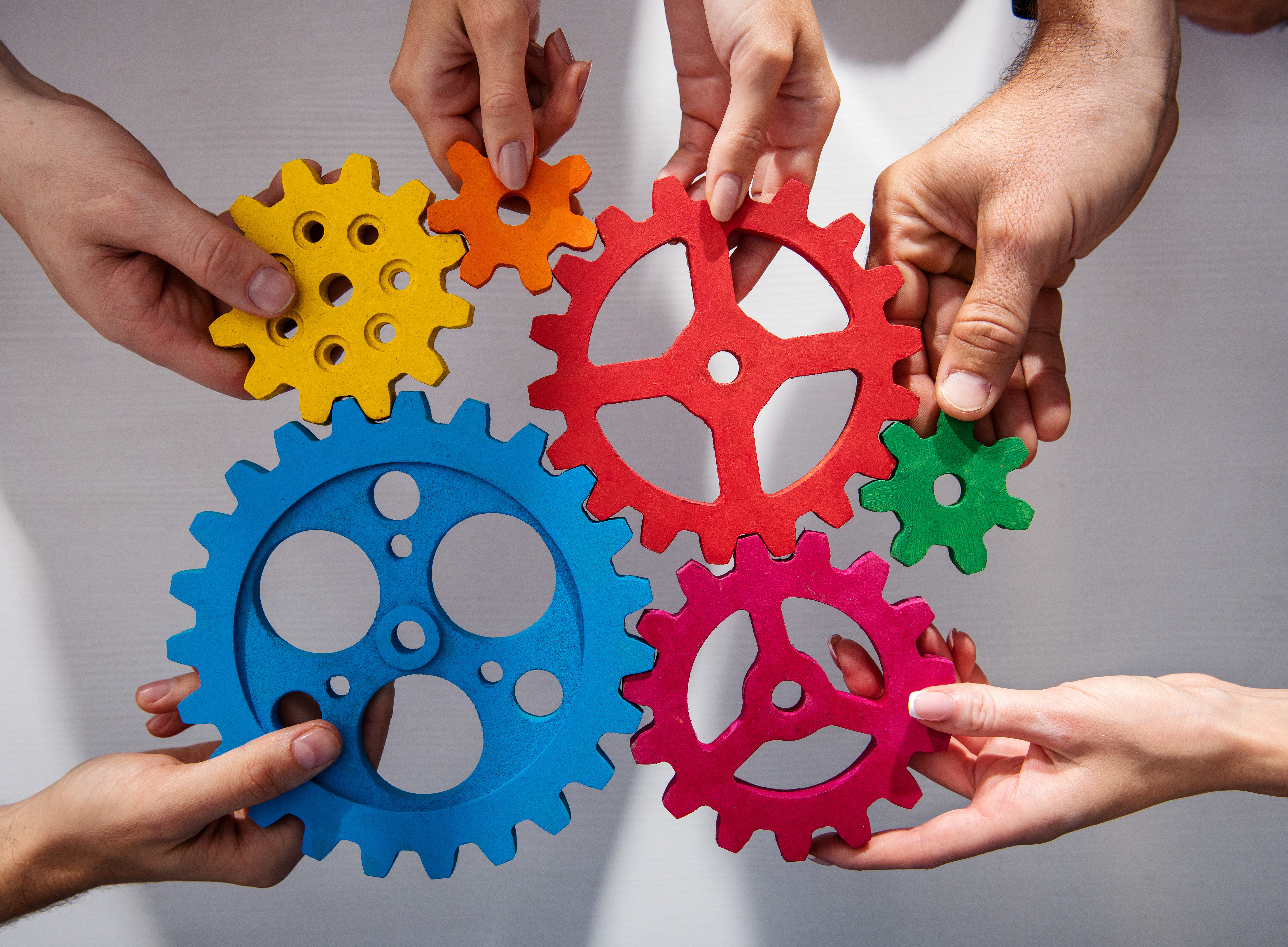 verschiedene Hände die bunte Zahnräder ineinander einrasten ©Alphaspirit - stock.adobe.com
