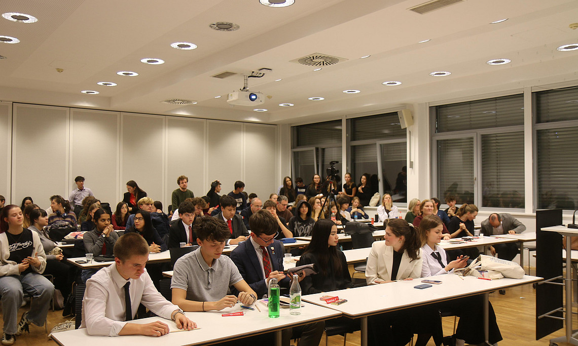 Jugendliche im Großen Hörsaal des UZT, im Vordergrund sitzen die 2 Finalisten-Teams nebeneinander und warten auf den Ausgang bzw. die Bewertung des Finales