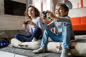 boy and girl playing video game console using controller while sitting at home